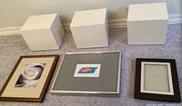 Three white display cubes with frames in front on carpeted floor.