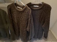 Two thick Irish pure wool cable knit sweaters, one brown and one dark brown, hanging side by side.