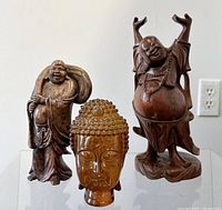 Front view of 3 Buddha figurines: two carved wooden statues and one amber-colored Buddha head