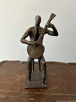Front view of bronze seated musician playing guitar, on a square base