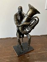 Front-right three-quarter view of bronze sculpture showing seated tuba player and bell orientation.