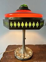 Lamp front view showing red glass shade, green glass panels and metal base.