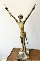 Front view of bronze Don Quixote statue with arms raised and marble base.