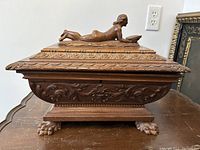 Front view of carved wood box showing overall design, lion claw feet, and reclining nude lady on lid