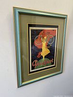 Front angled photo of the framed vintage bicycle advertising print showing the woman holding a bicycle overhead with visible colors and frame details.