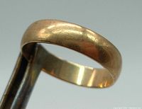 Close-up of the gold band ring showing its plain smooth design with light scratches and vintage wear.