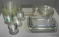 Wide view showing a mix of large round casserole dishes with lids, rectangular and oval baking dishes, and an assortment of clear glass bowls with ribbed sides.