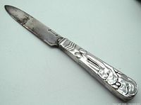 Antique letter opener with decorative Art Nouveau handle, signed Victoria, showing blade with patina and wear.