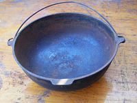 Photo showing top view of cast iron Dutch oven with wire bail handle, interior surface visibly rusted and worn.