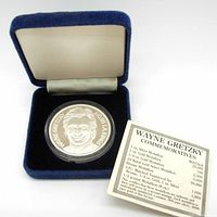 Silver coin displayed inside blue velvet-lined display case alongside informational card about Wayne Gretzky commemoratives