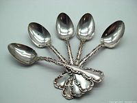 Set of five sterling silver teaspoons with ornate handles fanned out, showing front and side views of the bowls and handles.