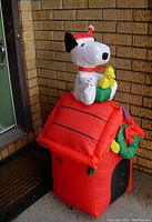 Peanuts Snoopy and Woodstock inflatable on red dog house with Christmas wreath and lights decorations, set up outdoors by front door.