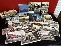 Wide view of an assortment of vintage postcards laid out on a flat surface showing many black and white and color images of architectural and landscape scenes.