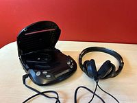 Open JVC Discman player with wired headphones resting beside it showing control buttons and LCD display.