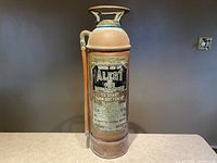 Front view of antique brass fire extinguisher labeled 'Alert', showing detailed operational and recharging instructions.