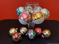 Front view of six glass ornaments and five plastic ornaments displayed with the glass ornaments hanging and plastic ones resting.