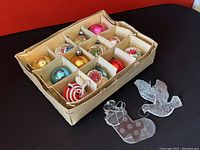 Photo of box containing 12 glass Christmas bulbs and 3 separate ornaments including plastic and metal bells.
