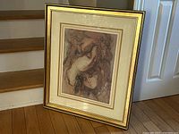 Framed lithograph leaning against stairs showing full artwork and frame with gold edges.