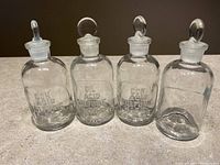 Four clear glass bottles side by side with oval-handled stoppers on countertop