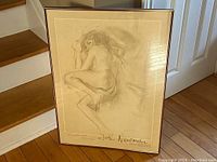 Framed signed lithograph leaning against stairs and door, showing full artwork and frame.