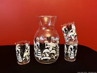 Front view of juice pitcher with three matching juice glasses decorated with black and white mushroom pattern against a red background.