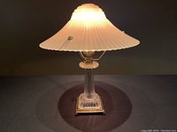 Front view of the Art Deco lamp lit, showing the pink glass shade and clear glass column base with brass accents.