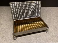 Open lid showing textured silverplate lid interior and shiny brass ribbed interior for cigarette storage with decorative claw feet on the box base.