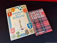 Photo of both Historical Map of Scotland and Scottish Clans & Tartans book placed side by side on a dark surface.