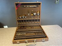 Overview of the open rosewood box displaying the full 58-piece flatware set arranged in rows including spoons, forks, knives, and serving utensils.
