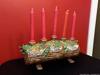 Front view of vintage ceramic yule log candelabra with five red taper candles and holly leaf decoration against red background.
