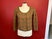 Front view of a brown wool tartan button-up sweater with three fabric-covered buttons on a dress form.