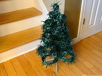 Full view of vintage tinsel Christmas tree with circular hoop branches on metal tripod base, showing overall shape and color.