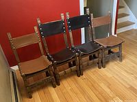 Photo showing all four Spanish carved wooden chairs, two with tan leather and two with dark brown leather, arranged in a row, highlighting their overall design and contrasting leather colors.
