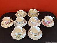 Full set of 8 antique vintage tea cups and paired saucers arranged on surface showing variety of floral and decorative patterns.
