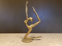 Front and side view showing the entire brass dancer figurine in an acrobatic pose on flat surface with plain background.