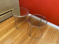 Two mid century modern nesting tables with chrome bases; larger table has a mirror top, smaller has smoked glass top.