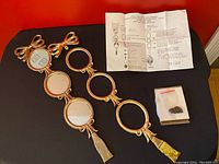 Four linked oval brass picture frames arranged vertically, noted one disassembled frame and instruction manual laid out on black surface.