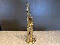 Front angled view of brass coin sorter tower bank with four graduated vertical tubes of varying heights on a round base.