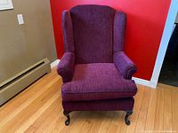 Front view of the French wingback lounge chair showing maroon upholstery and wooden legs on a hardwood floor.