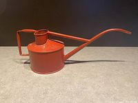 Side profile of the red Haws antique watering can showing cylindrical body, long spout and upright handle with fill opening on top.