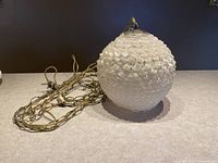 Lucite ribbon lamp shade with attached gold-tone chain on counter, showing textured Lucite detail and wiring.