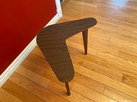 Full view of boomerang-shaped walnut veneer end table, showing the wood grain and three tapered legs.