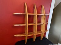Front and side angled view of the Mid Century Modern pine floating shelf against a red wall, showing its overall design, wood grain, and construction details.