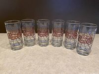 Six clear glasses in a row, each with a red Pepsi-Cola logo and blue geometric lines