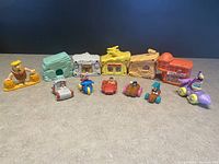 Overview of six pastel colored Flintstones village houses and six character cars with figures