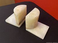 Two vintage agate stone bookends on black surface with red background, showing both semi-cylinder and base sides.