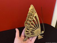 Front view of vintage brass butterfly napkin holder held in hand showing intricate wing details and wire antennae.