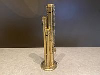 Front and angled view of the vintage brass coin counter with three tubes for quarters, dimes, and nickels. Shows the locked padlock and chain securing the tubes.
