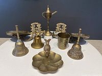 Photo showing all the vintage brass items including sconces, bells, bird dish, brass cup, and pitcher-shaped item grouped on a white surface