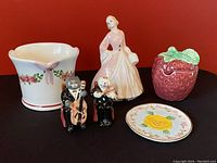Overall lot showing pink dress figurine, strawberry jam jar, cat salt and pepper shakers, small vase, and plate.